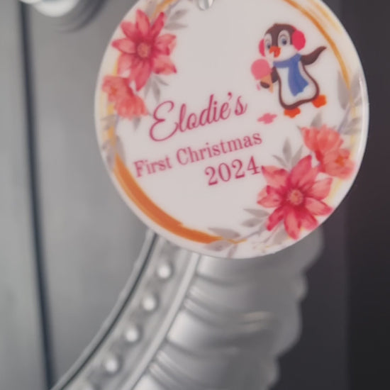 Video of a round ceramic ornament with a cute penguin and pinky peach flowers celebrating babys 1st Christmas