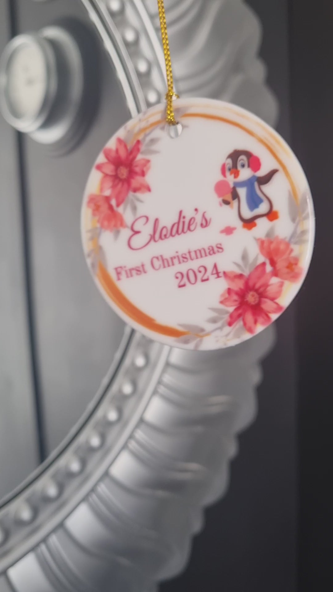 Video of a round ceramic ornament with a cute penguin and pinky peach flowers celebrating babys 1st Christmas